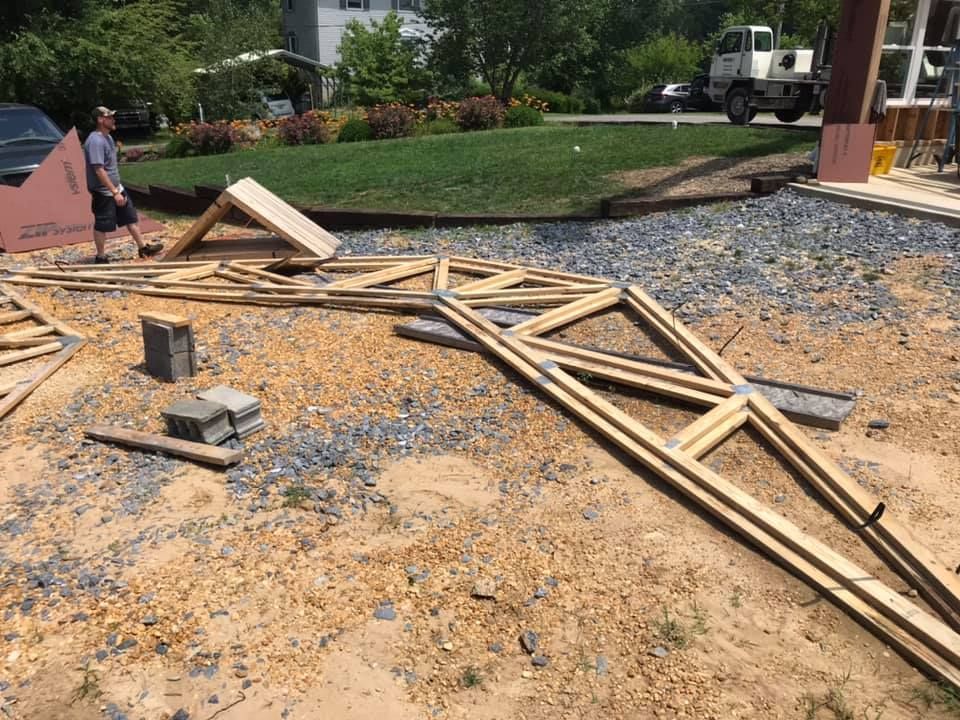 Collapsed wooden frame and debris scattered across a gravel driveway near a house