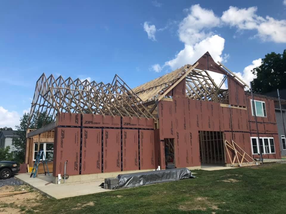 Partially built red house frame with exposed roof trusses under a blue sky