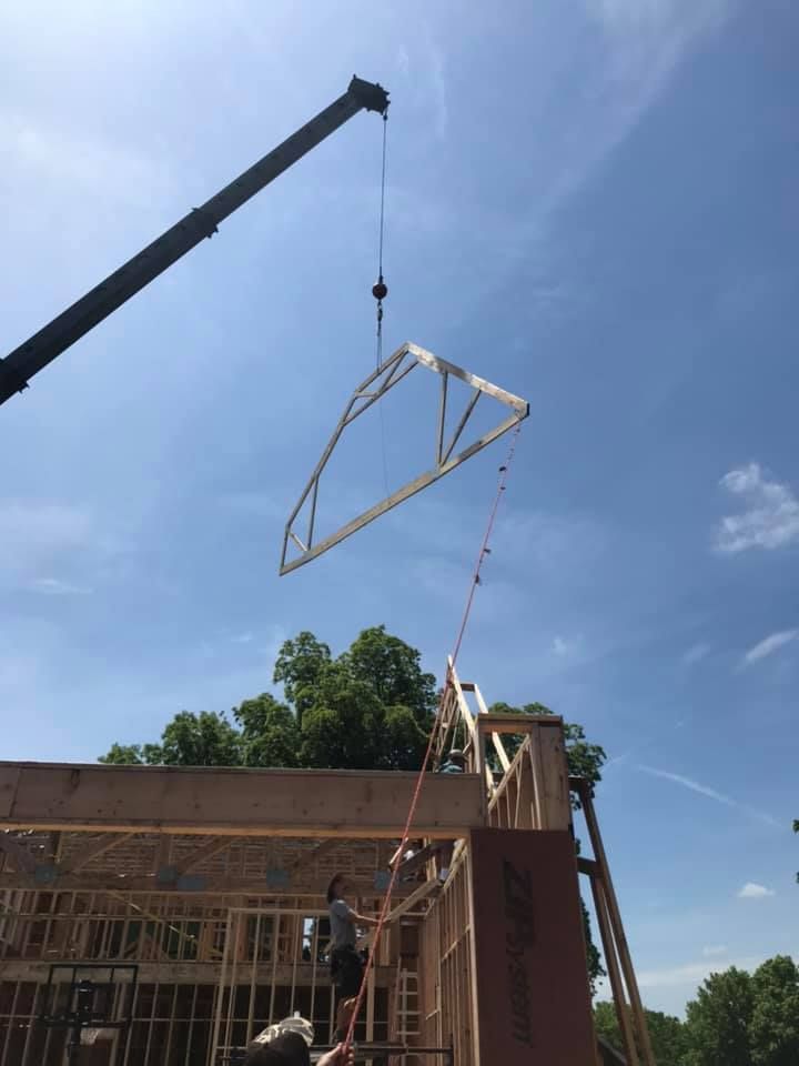 Crane lifting a roof truss over a building under construction on a clear blue sky.