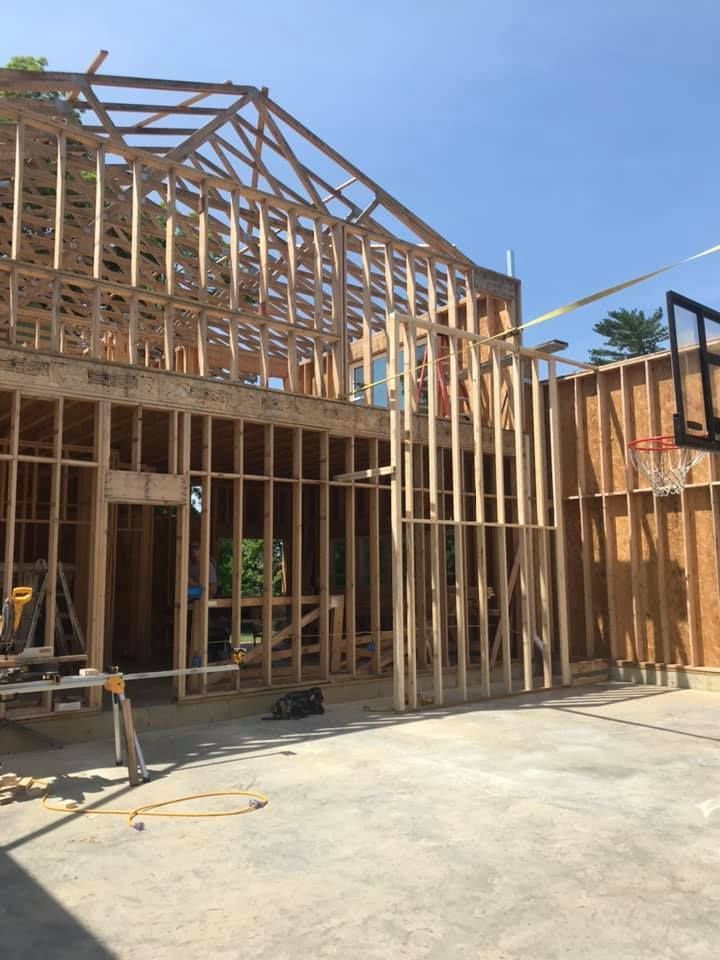 Framed house under construction with exposed wooden beams and a concrete slab in front