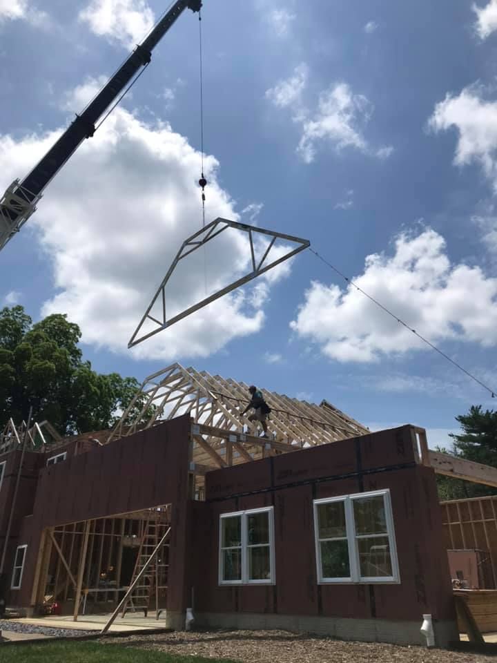 Crane lifting a roof truss onto a house under construction with a partly framed roof and windows.