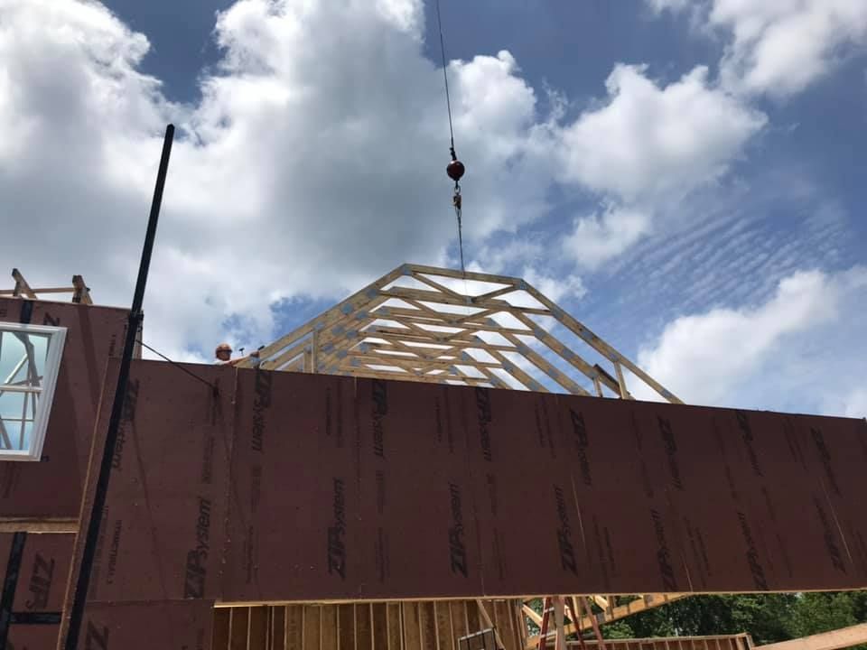 Crane lifting a wooden roof frame above a large red structure under a cloudy sky