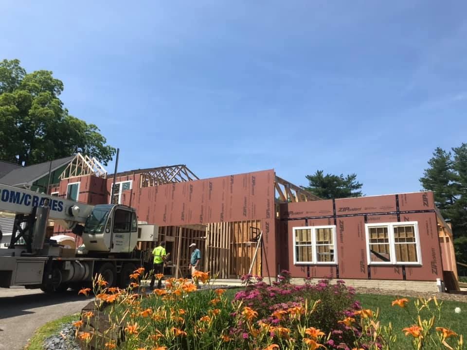 Construction crew erecting a small house frame beside a truck, with orange flowers in the foreground