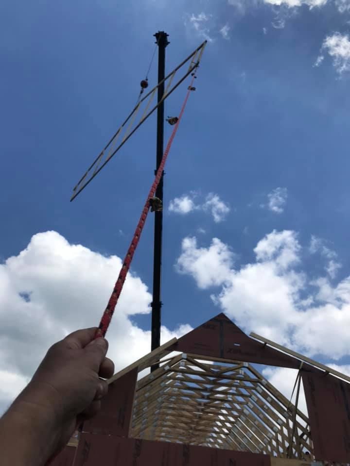 Hand holding a red pole with wires against a blue sky above a building roof frame