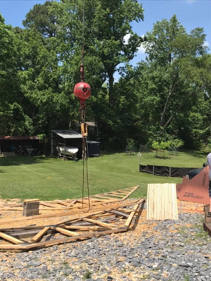 Red crane hoists a beam over a construction site with lumber and trees in the background