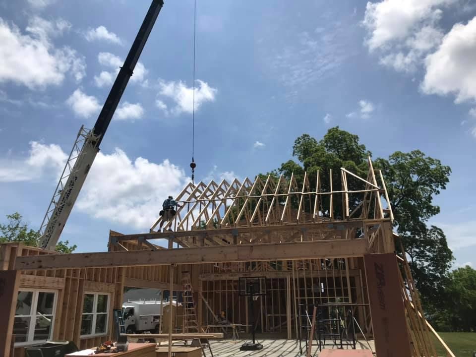 House under construction with a crane and wooden roof framing under a partly cloudy sky