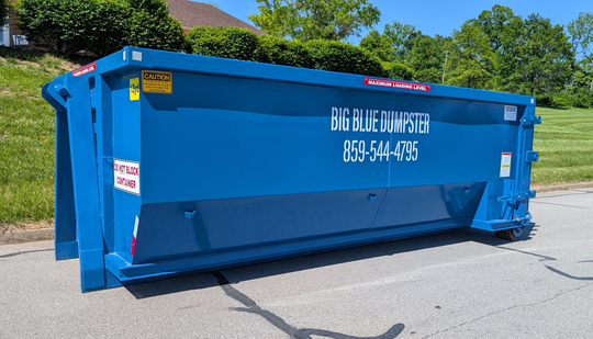 Blue construction dumpster on a roadside with white company lettering.