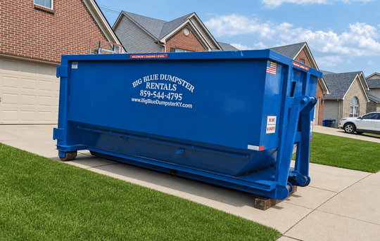 Blue dumpster on a driveway in front of a house, with white lettering on the side