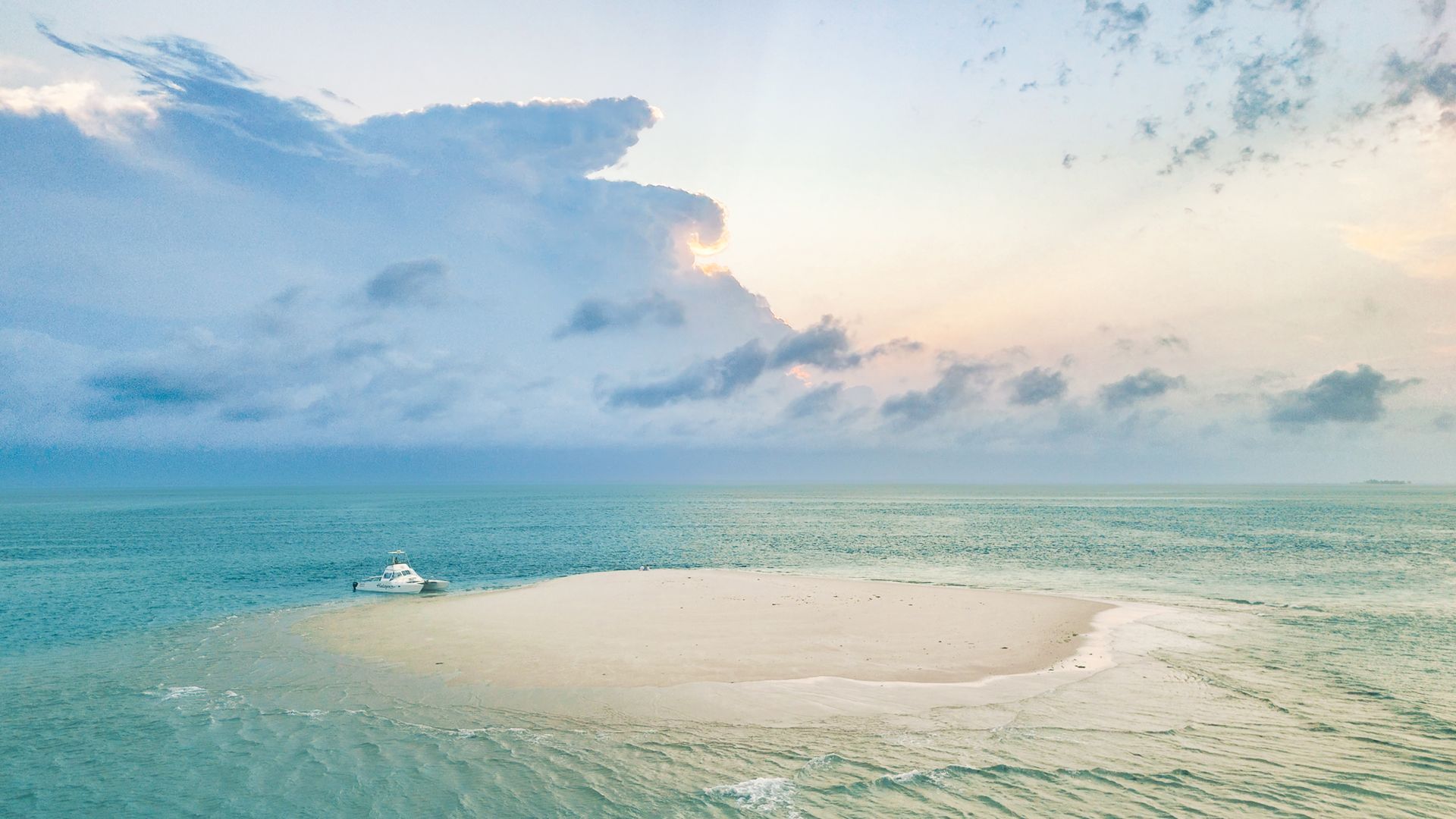 Aerial view of a shallow turquoise sandbar and calm sea under a pastel cloudy sky