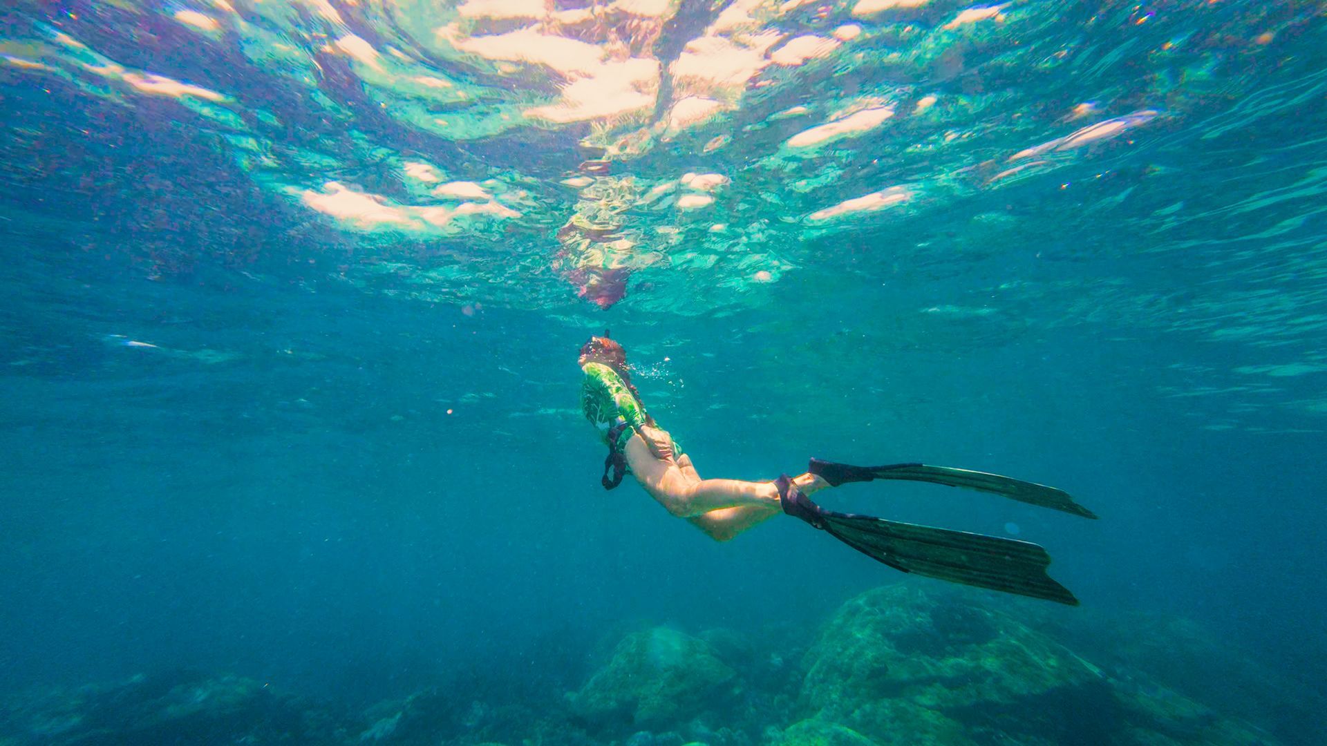 Snorkeler swimming underwater in clear blue ocean above a coral reef