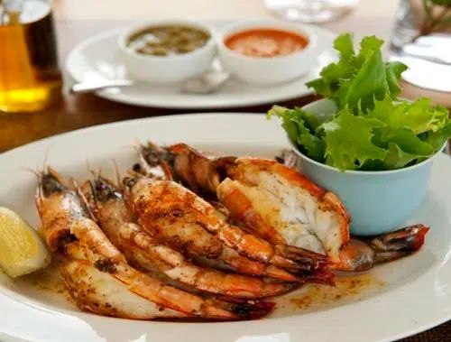 A plate of grilled jumbo shrimp served with a side of fresh lettuce and two small bowls of dipping sauce.