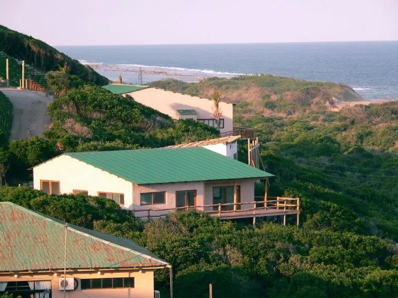 Houses with green roofs nestled among lush green coastal hills overlooking the ocean.