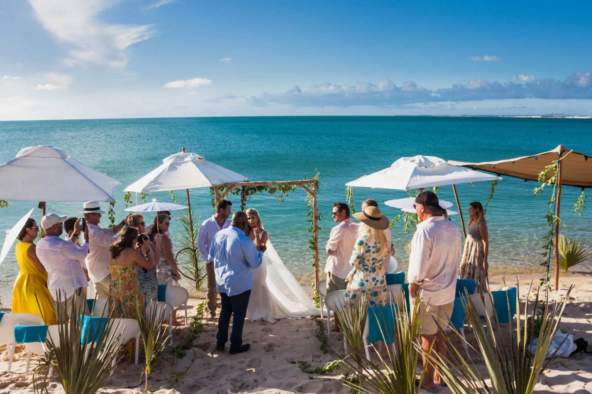 Beach wedding ceremony under white umbrellas beside turquoise ocean and sandy shore