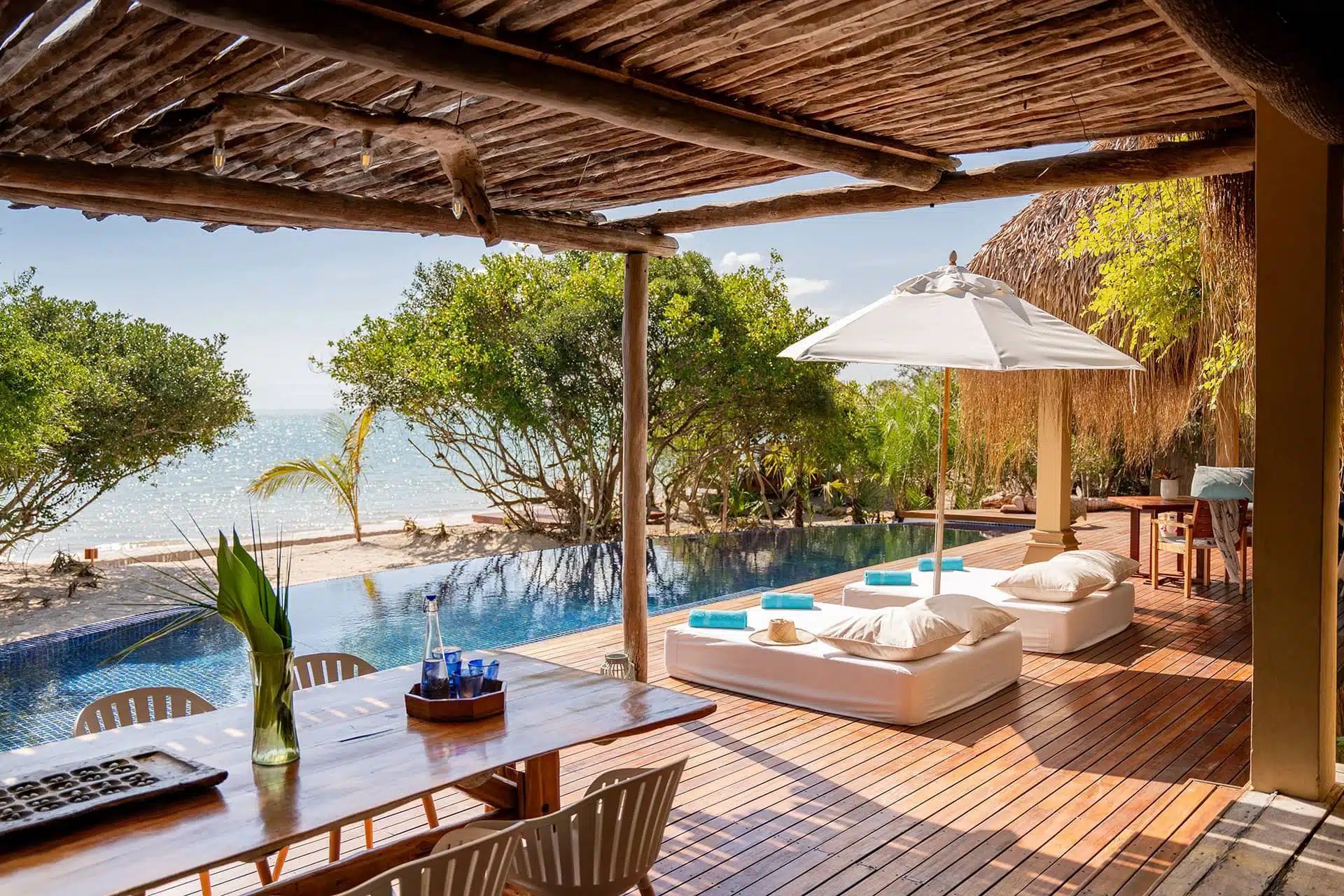 Beachfront lounge with white cabana beds, umbrella, and wooden deck overlooking the ocean