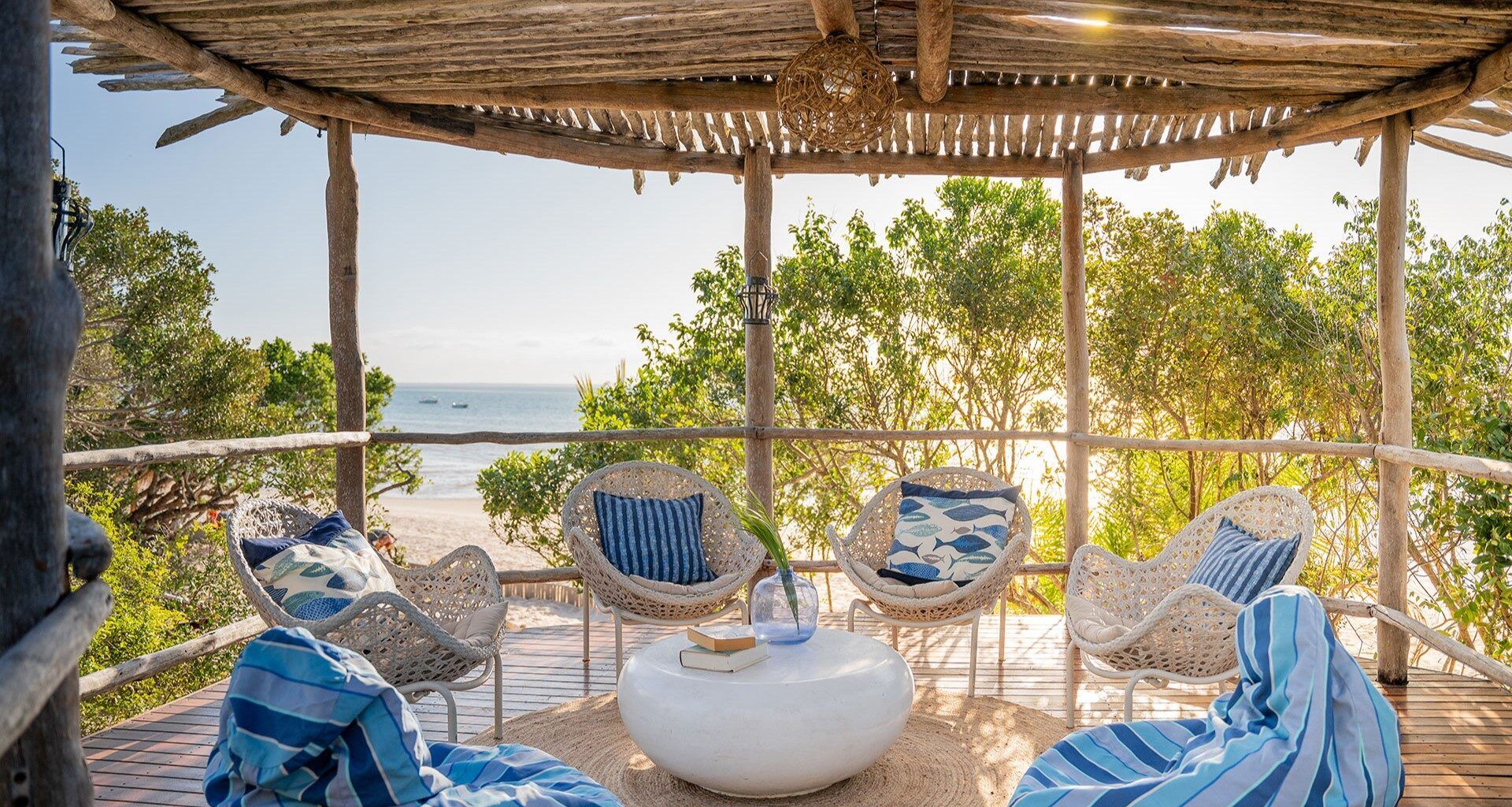 Tropical riverside lounge with wicker chairs, blue cushions, and a thatched roof overlooking the water