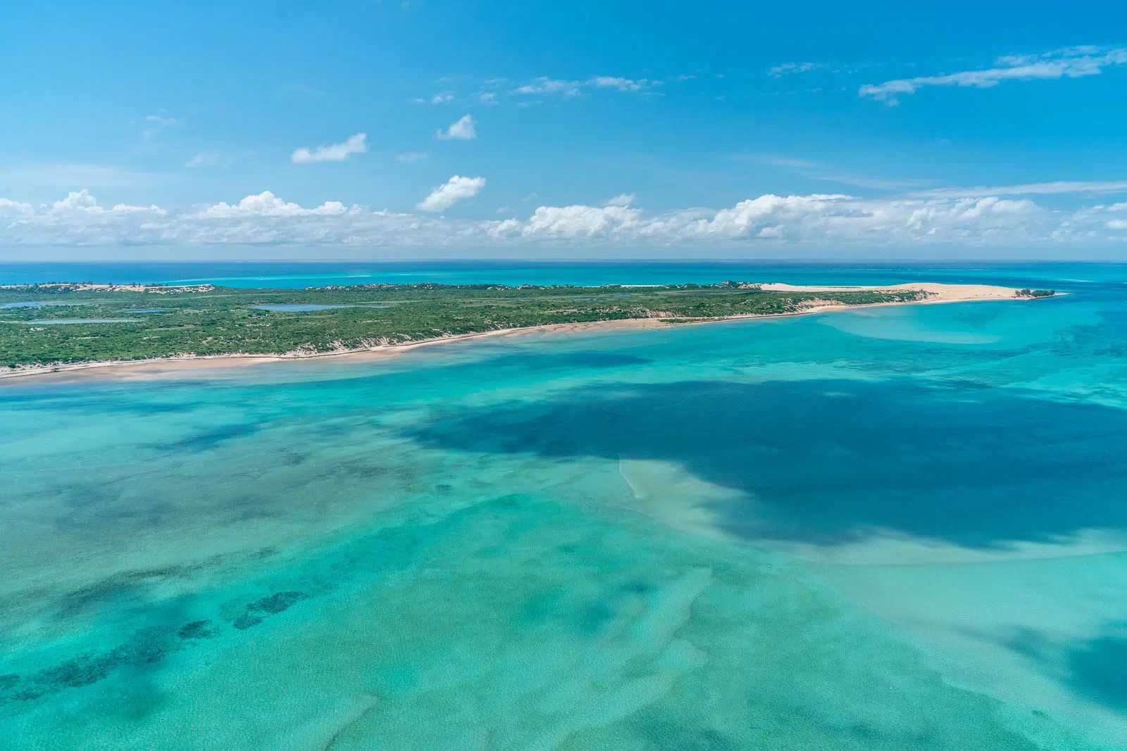 Aerial view of turquoise ocean and white sand coastline under a bright blue sky