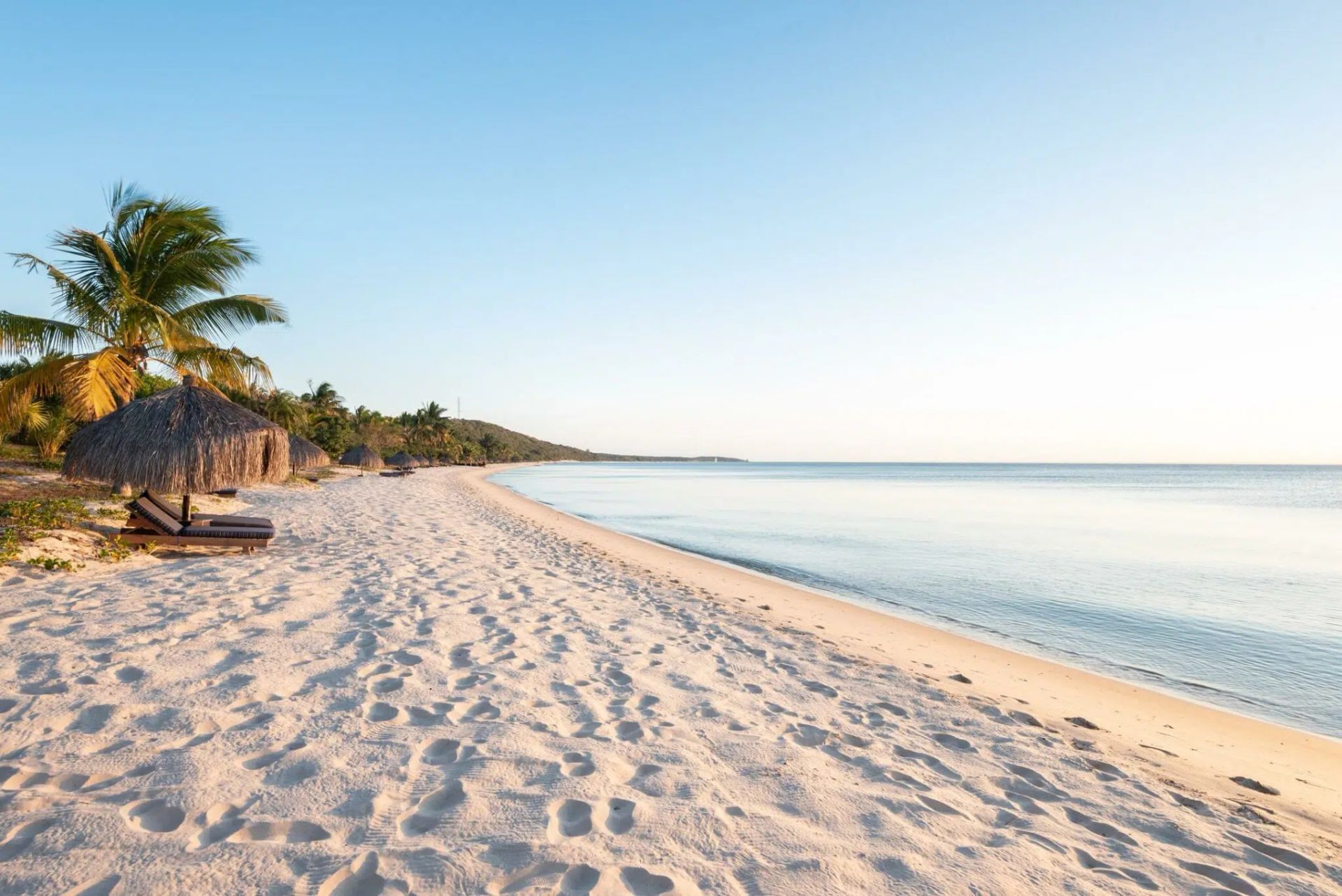 Sunny tropical beach with white sand, palm trees, and calm turquoise water at sunrise
