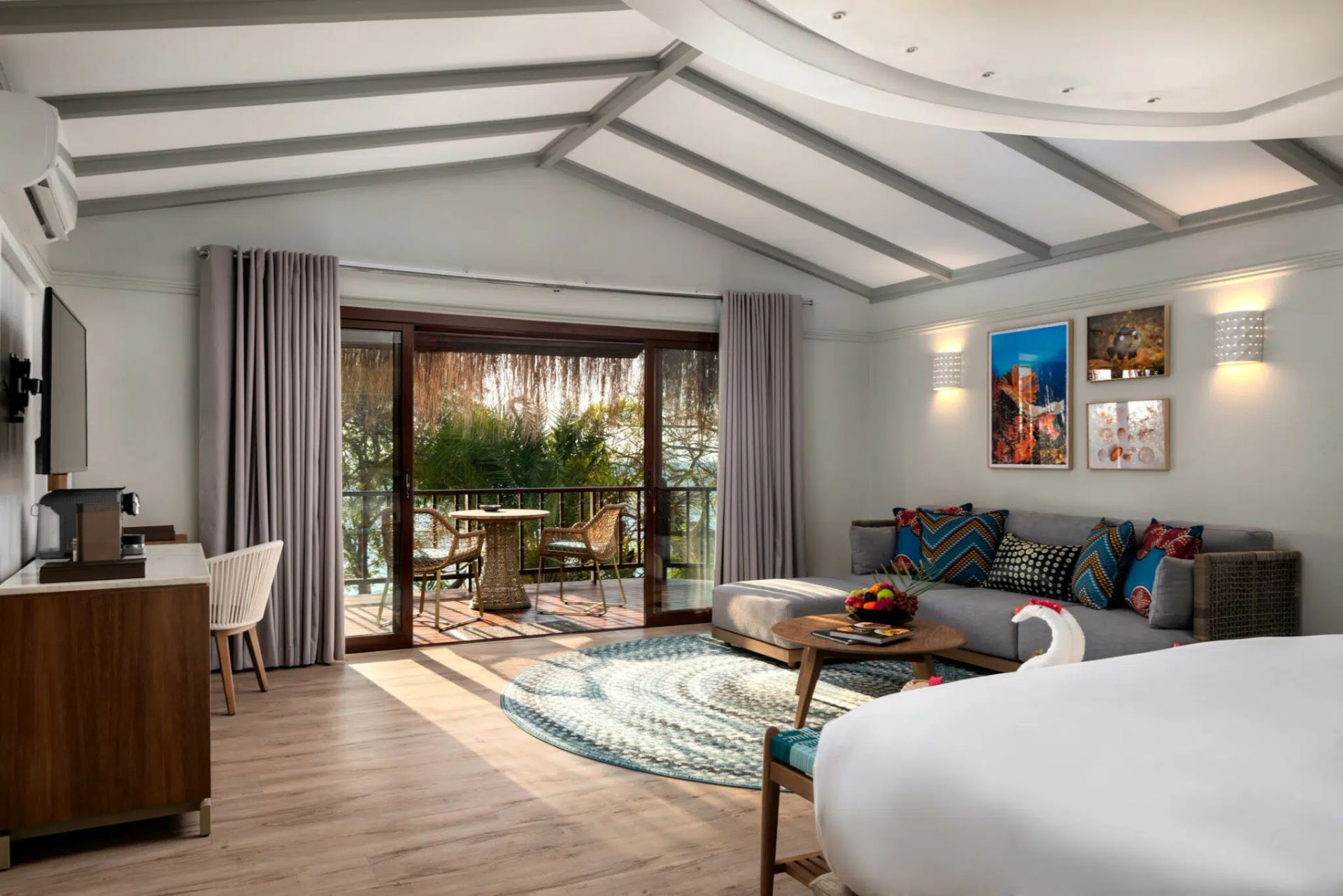Bright modern bedroom with balcony doors, striped sofa, desk, and bed in a coastal-style room