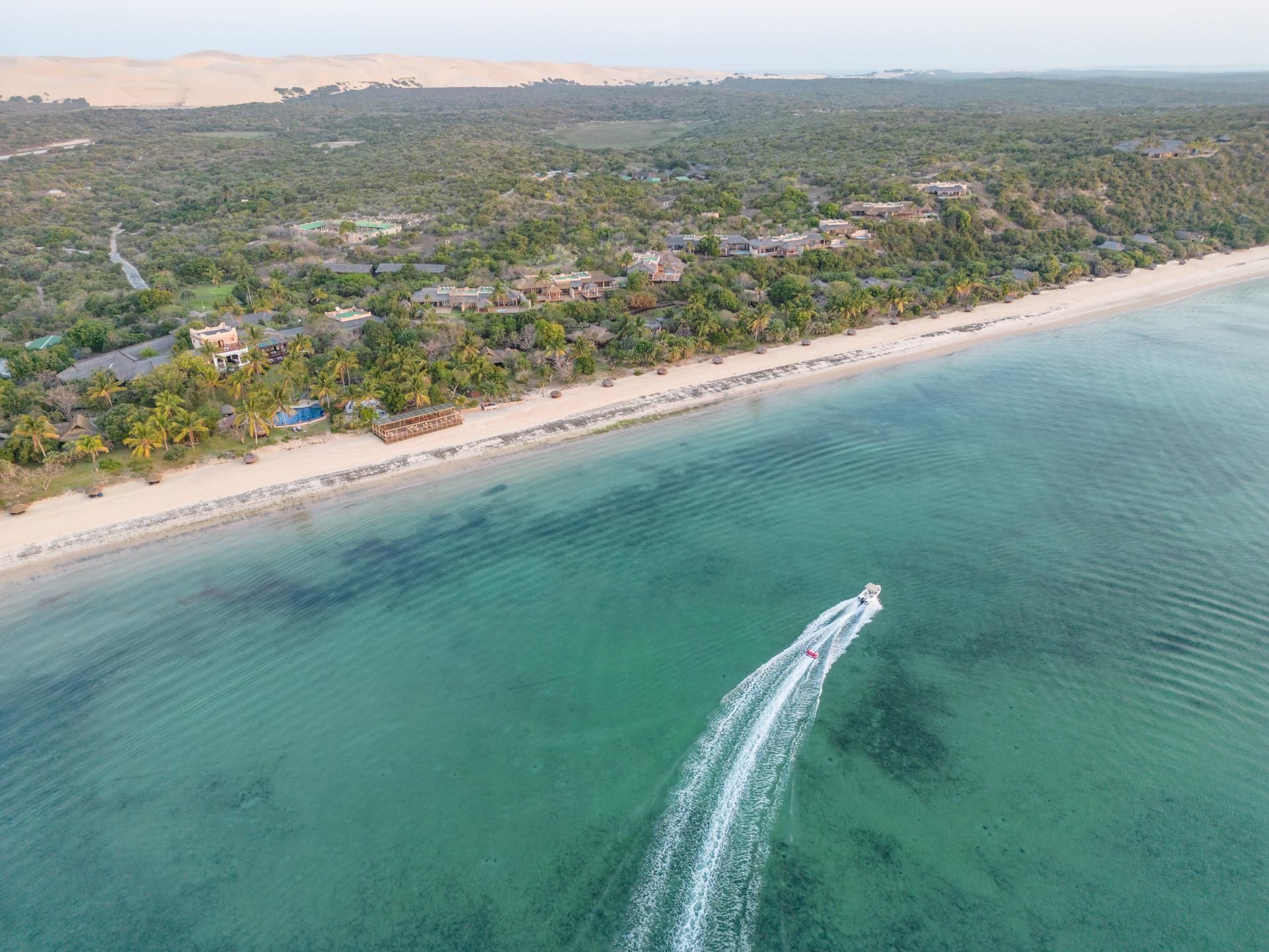Aerial view of a tropical beach with turquoise water, white sand, and a speedboat leaving a wake
