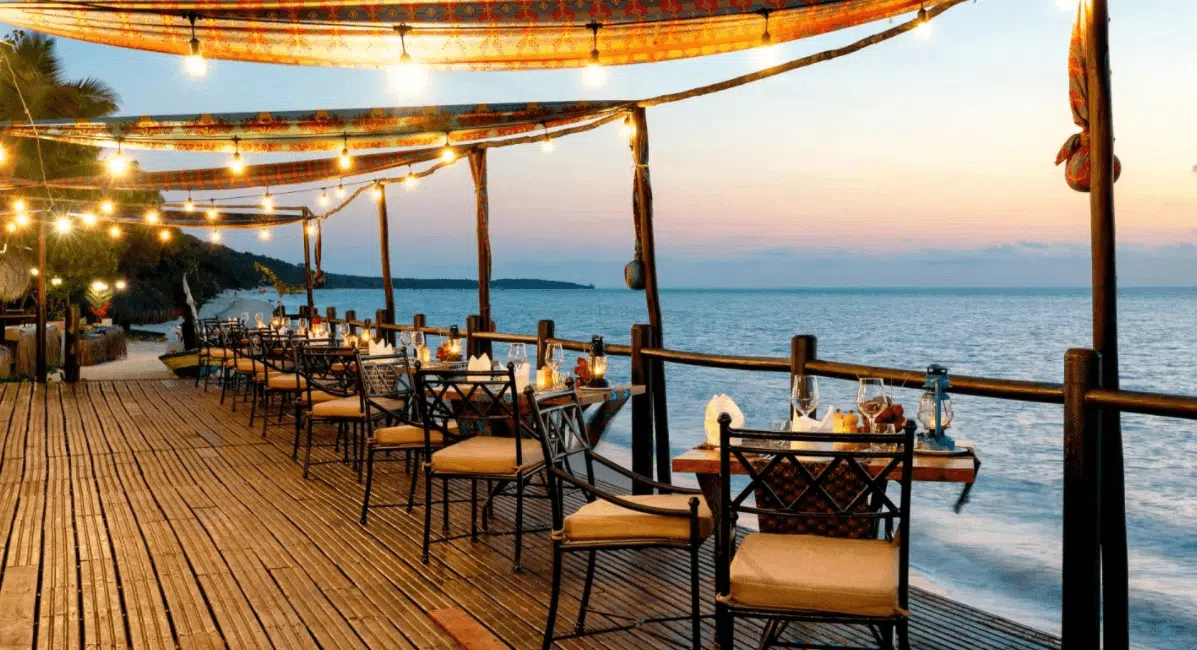 Seaside restaurant deck with tables and chairs under string lights at sunset overlooking the water