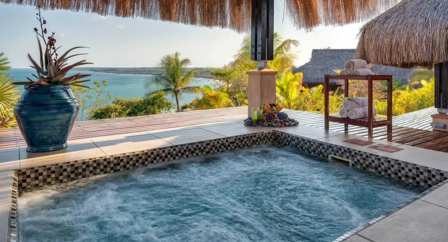 Private pool overlooking a turquoise ocean, with thatched cabana, palm trees, and sunset light