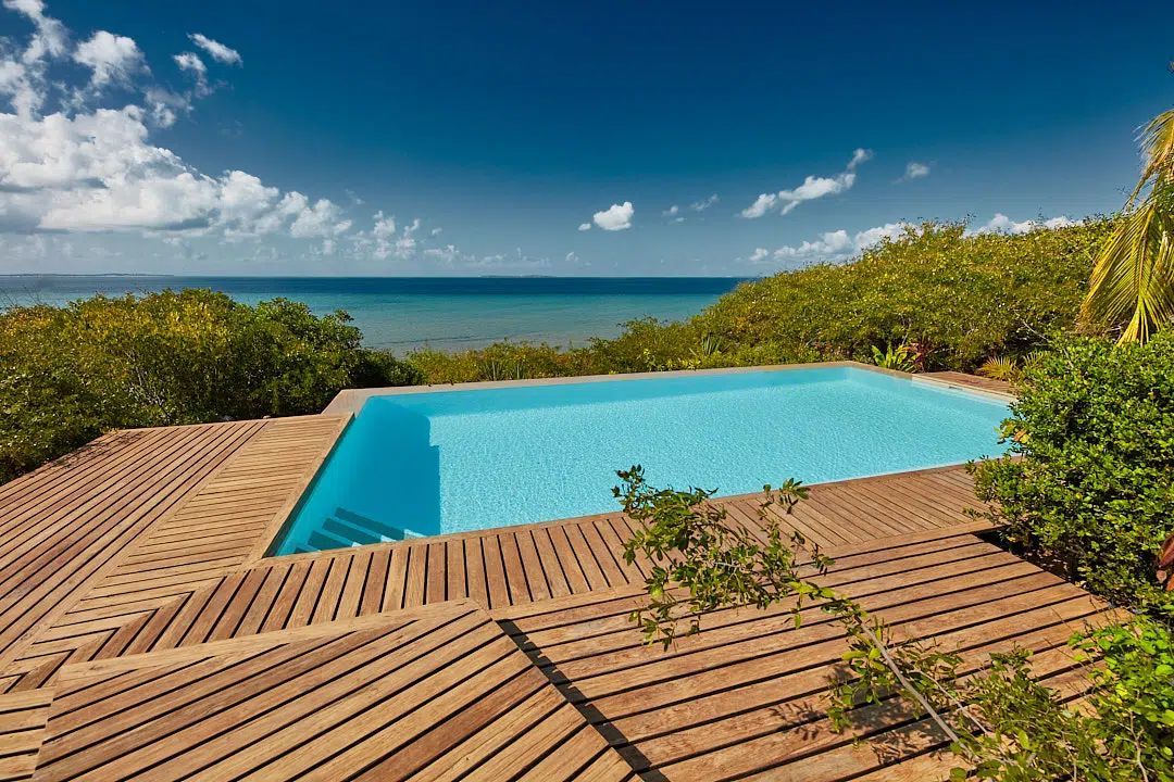 Infinity pool on a wooden deck overlooking the ocean under a bright blue sky