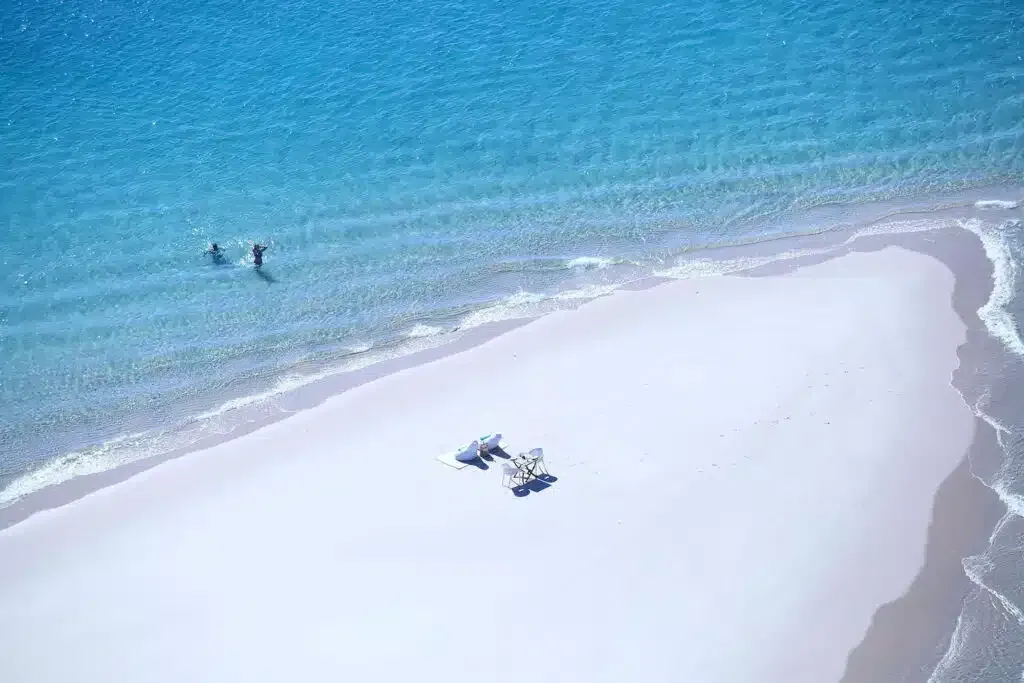 Aerial view of a white sand sandbar in turquoise water with a few people near the shore