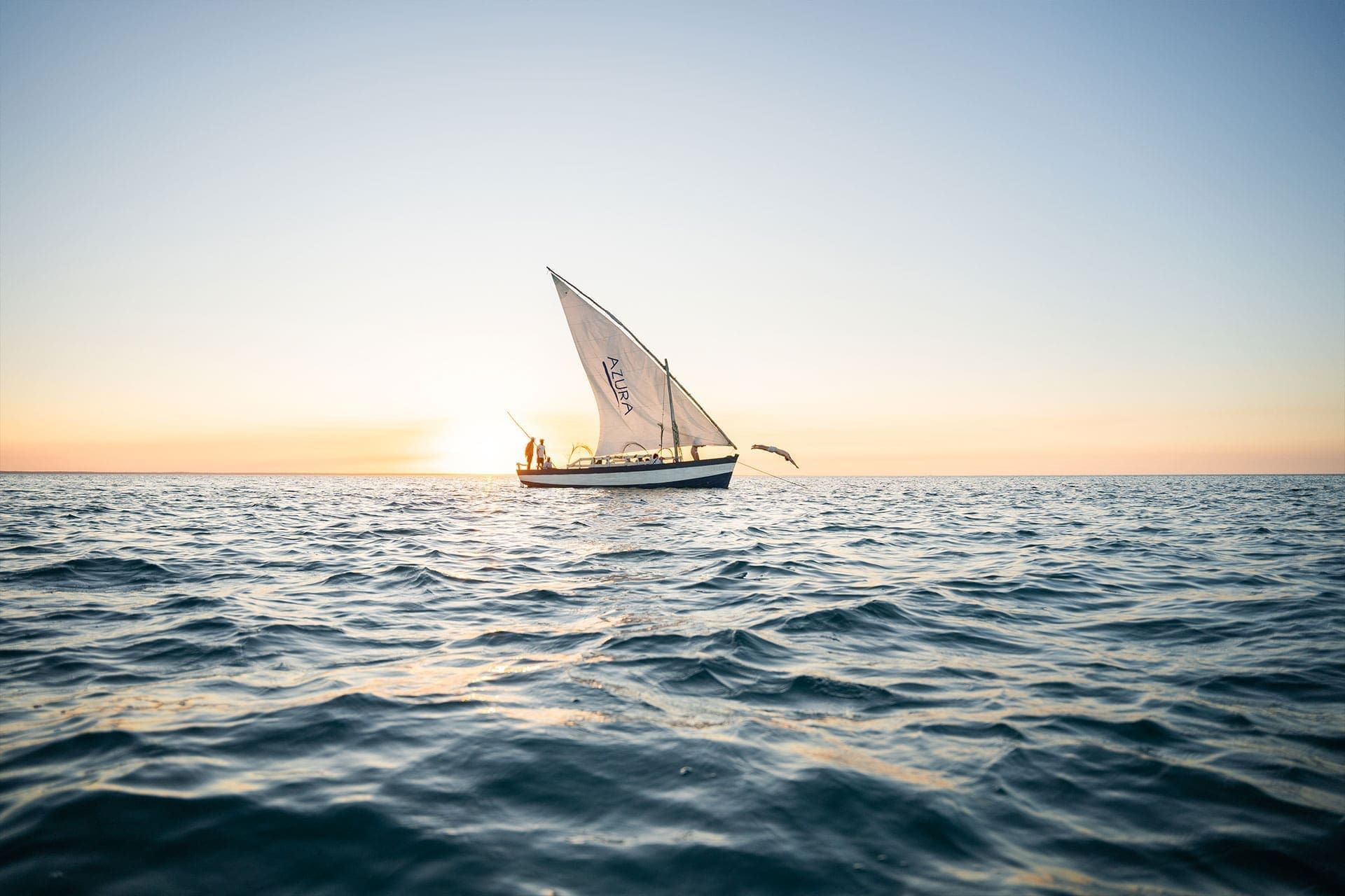 Sailboat on calm ocean at sunrise, with golden light on the horizon