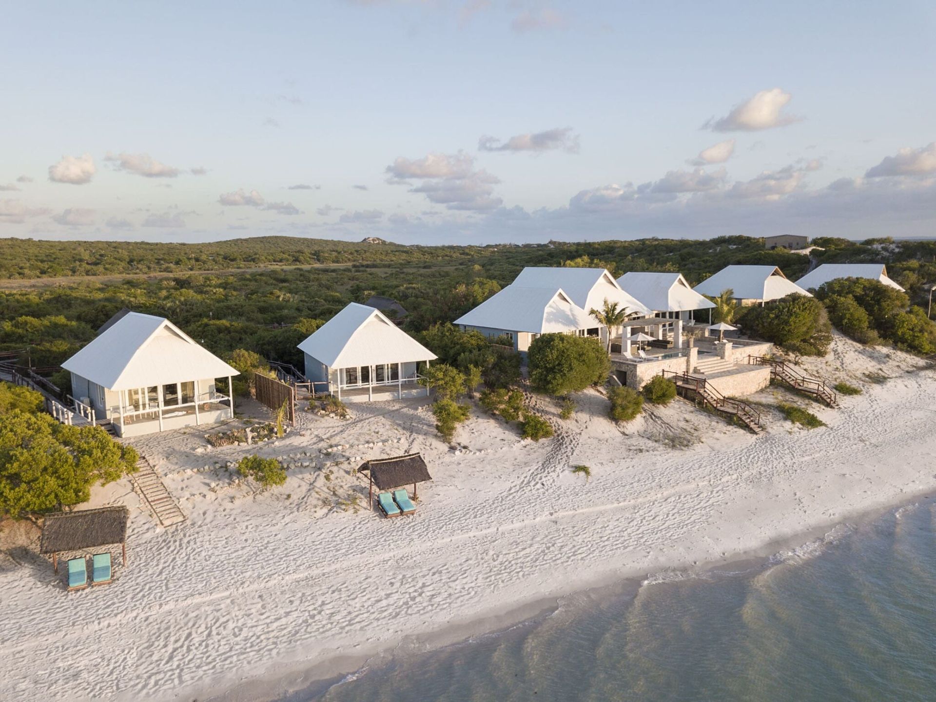 Aerial view of white beach cottages and huts on a sandy shoreline beside calm water and greenery
