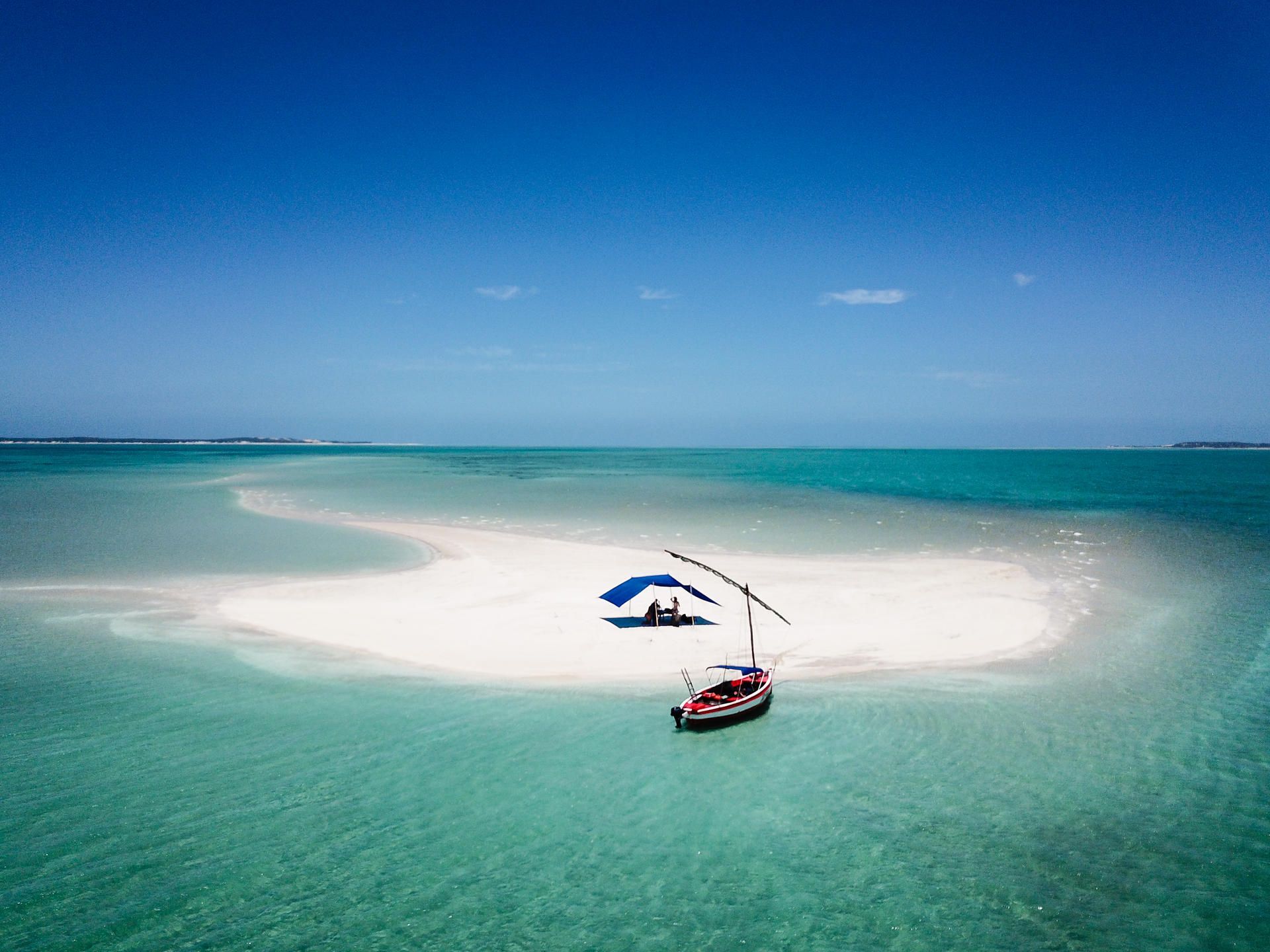 Small sailboat on a white sandbar in turquoise tropical water under a clear blue sky.