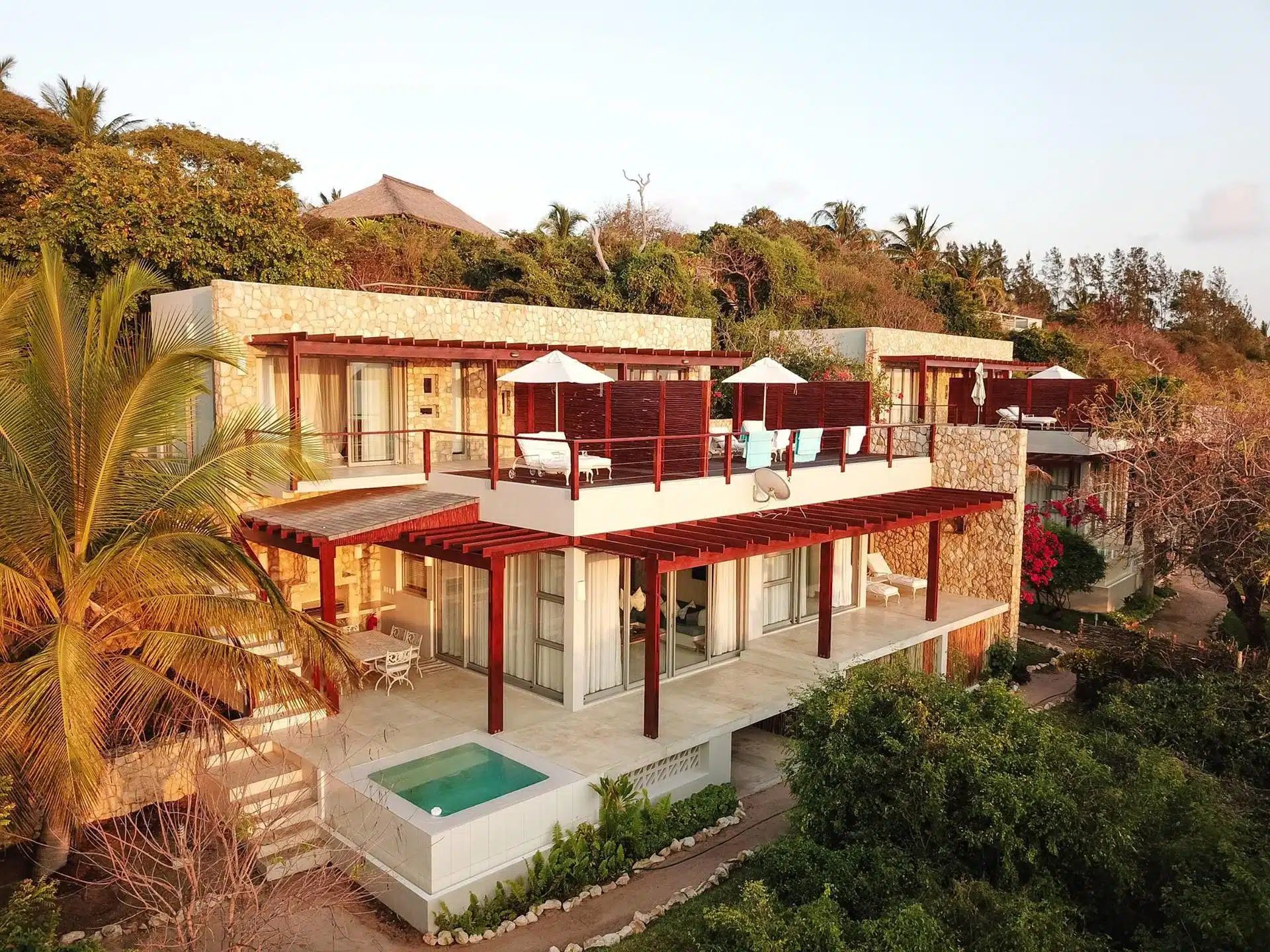 Modern hillside villa with red roofs, white walls, and a small pool surrounded by lush greenery