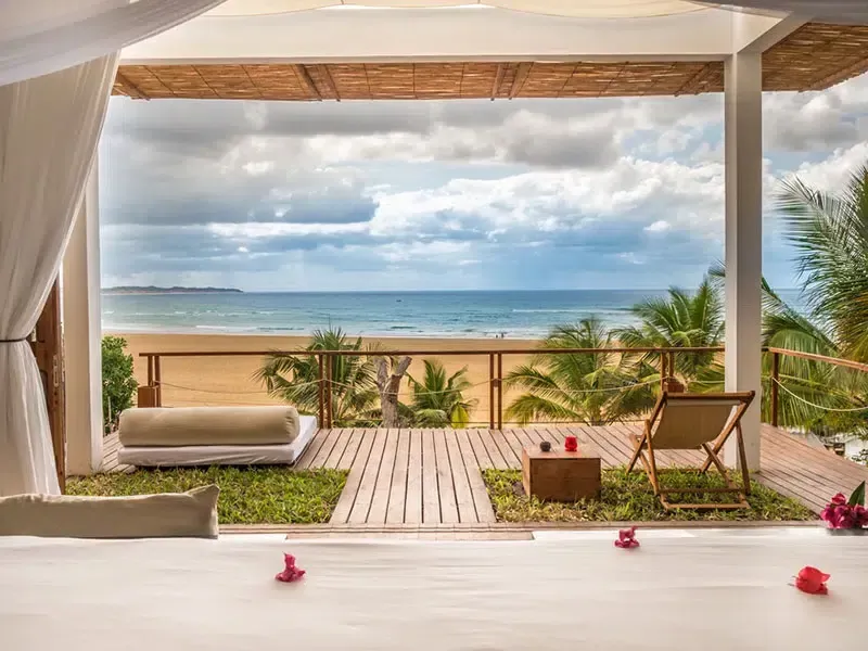 Palm-framed sandy beach with a turquoise lounge chair and calm ocean at sunset