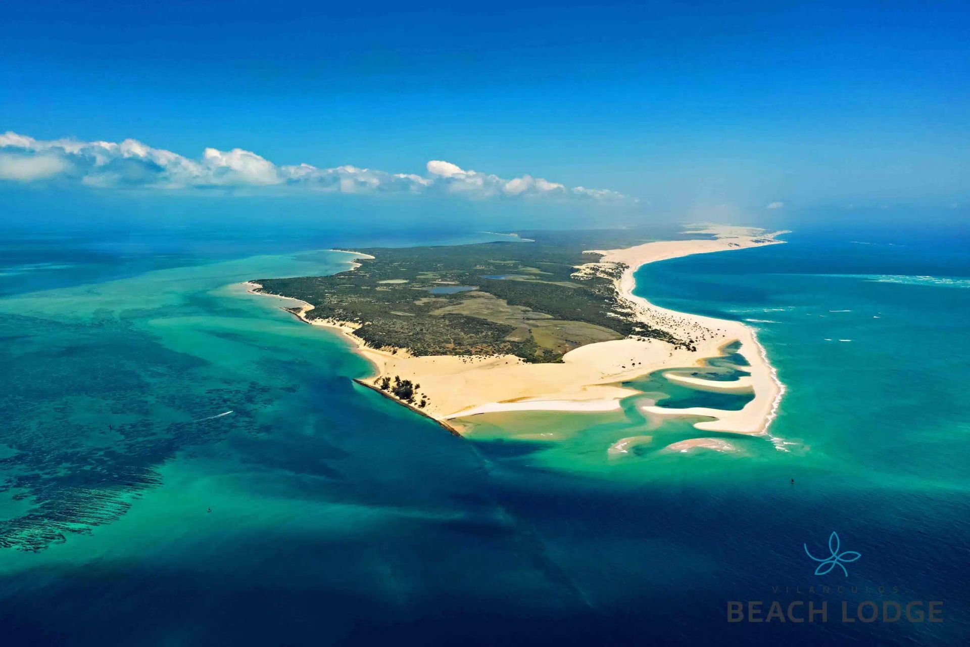 Aerial view of a tropical island with white sand beaches, turquoise water, and a cloudy blue sky