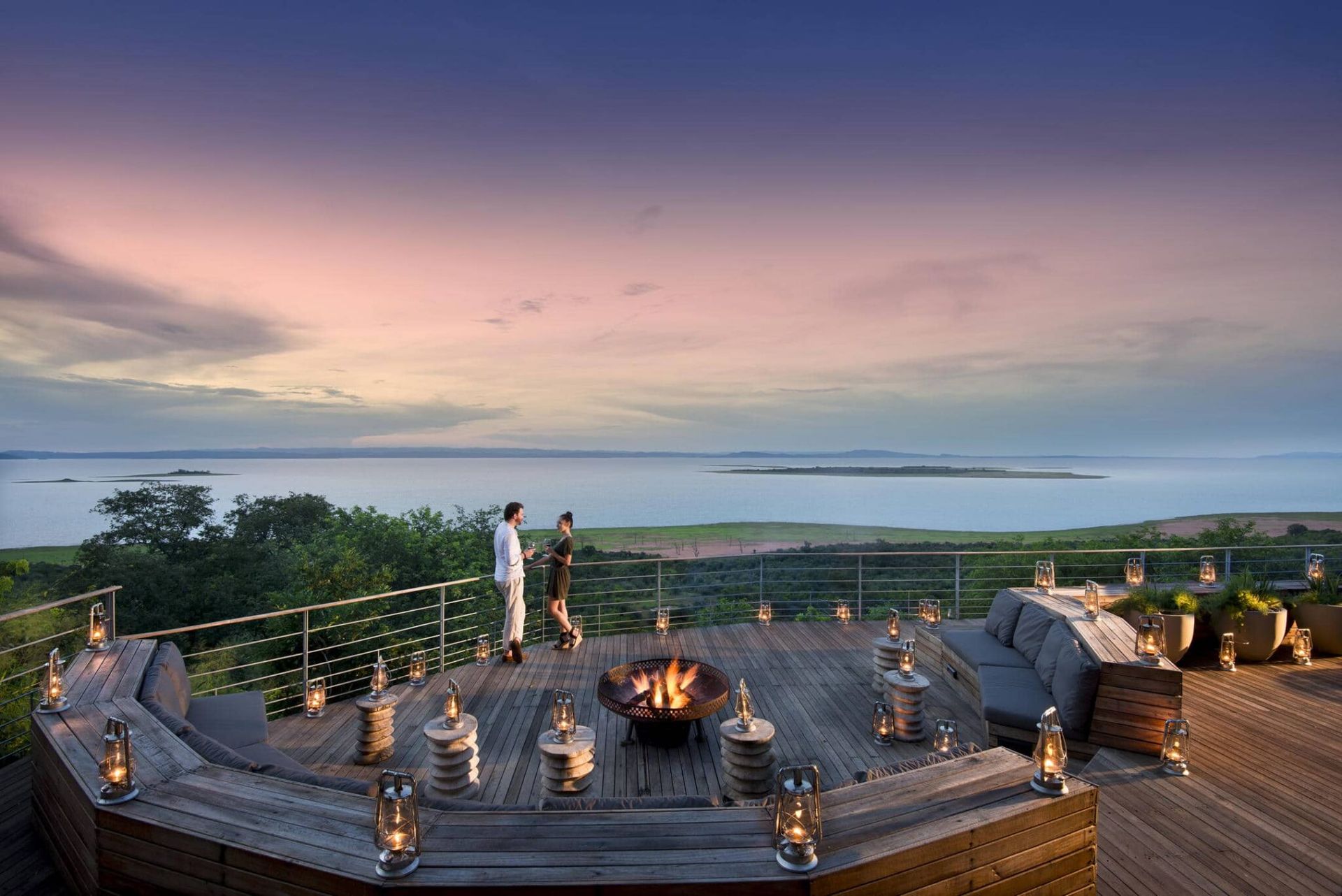 Sunset overlook with a fire pit, seating deck, and two people by the railing above the water