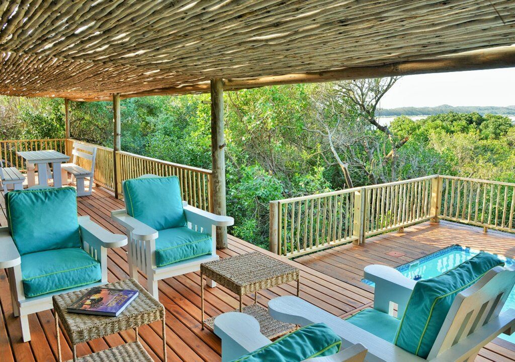 Outdoor deck with turquoise chairs, wooden table, and lush green valley view under a shaded pergola