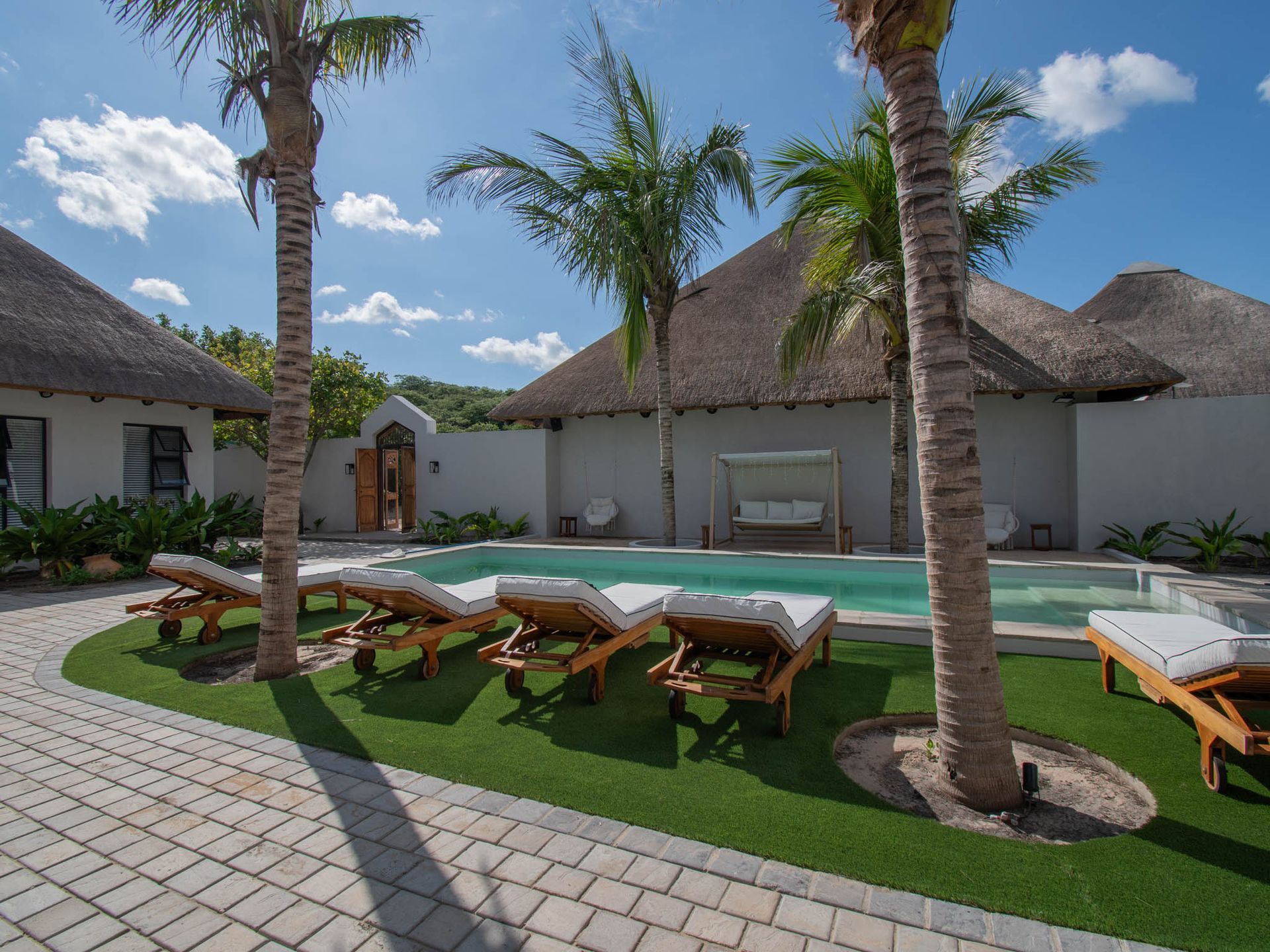 Tropical resort courtyard with palm trees, lounge chairs, and a pool under a blue sky