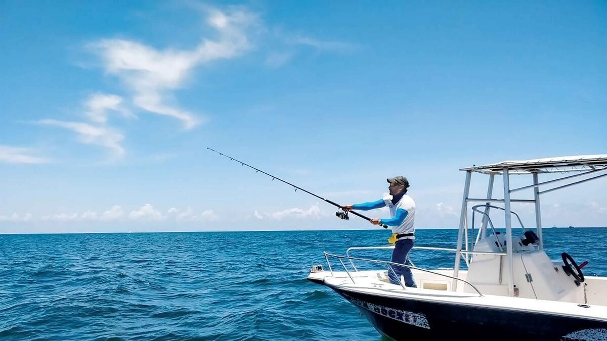 Person fishing from a white boat on a blue ocean under a clear sky
