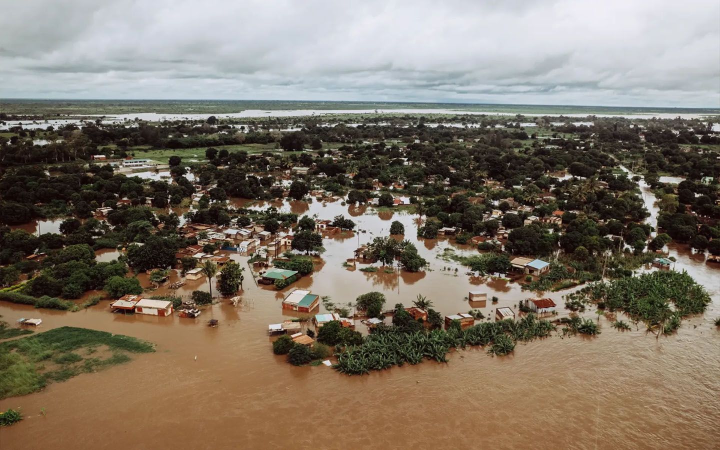 Flooded village with brown water submerging homes and trees under a cloudy sky