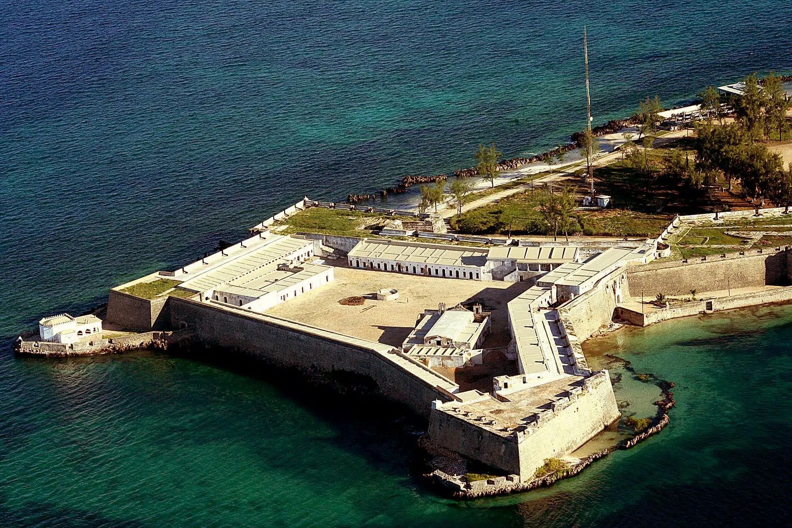 Aerial view of a stone coastal fortress on a rocky peninsula beside turquoise water