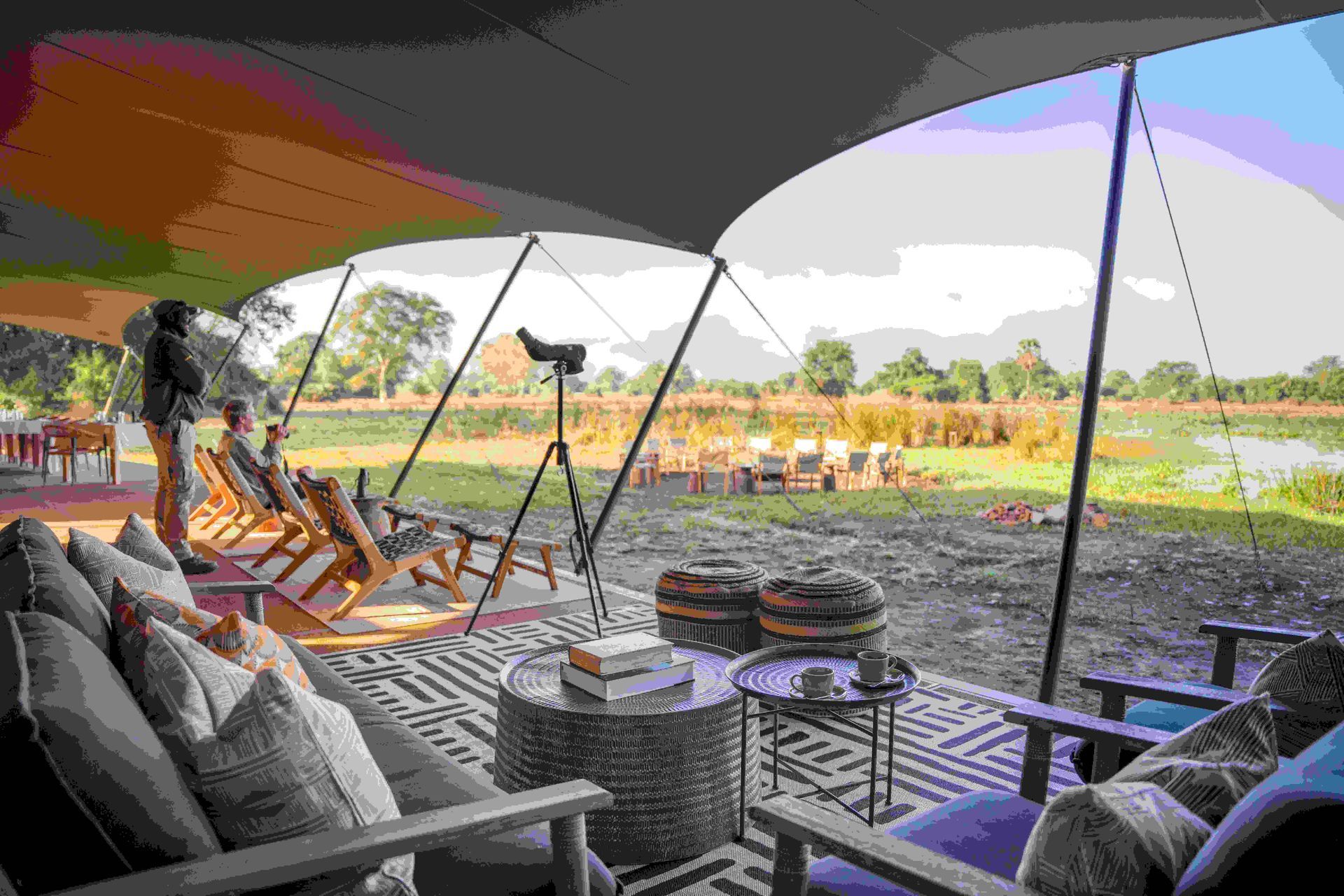Shaded outdoor lounge with chairs and tables overlooking a sandy beach and ocean under umbrellas