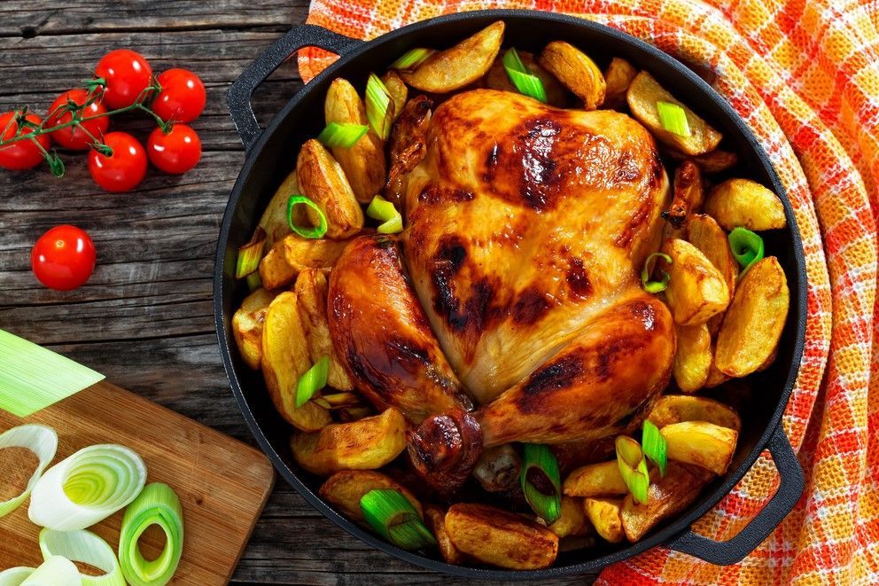 Roasted chicken in a cast-iron skillet with green onions and potatoes on a rustic table