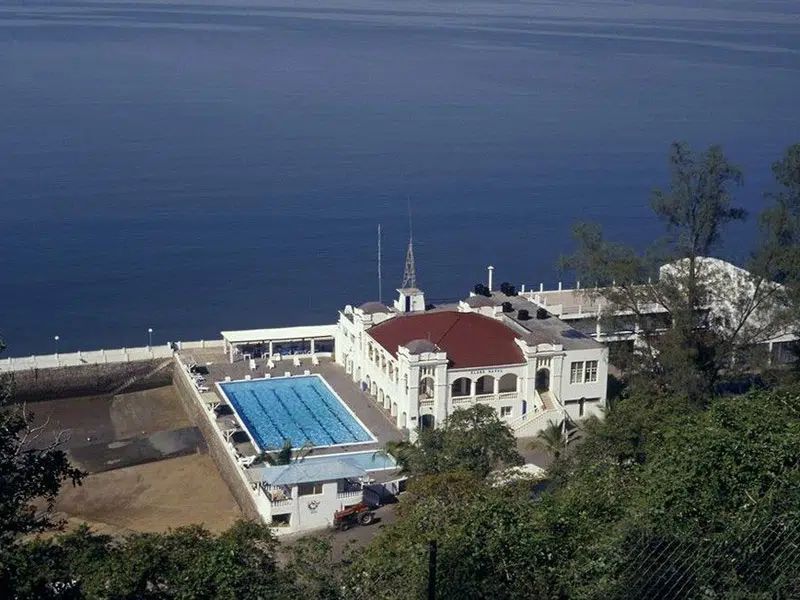 White seaside building with a red roof and blue pool overlooking the ocean