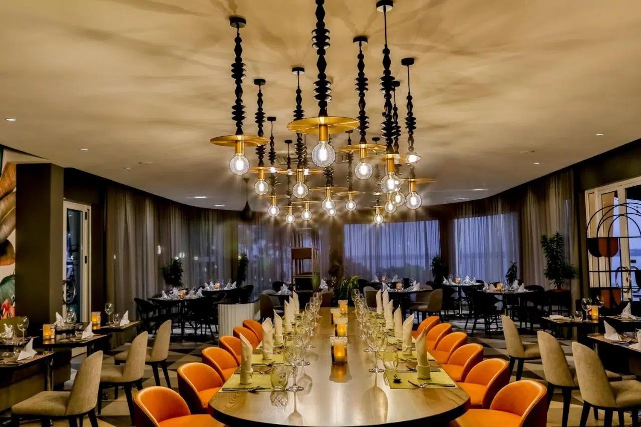 Elegant restaurant dining room with long table, orange chairs, chandeliers, and dark drapes