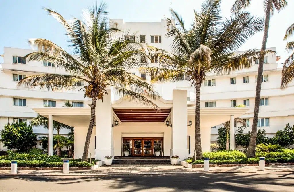 Modern white hotel entrance with palm trees and a driveway in front