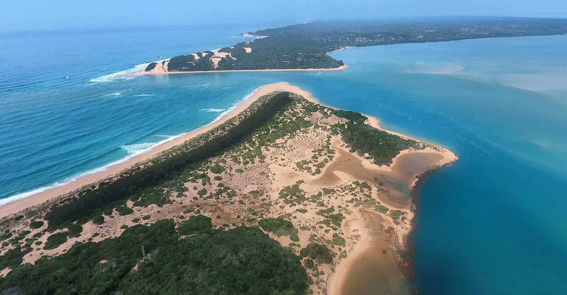 Aerial view of a sandy coastal peninsula with blue ocean on both sides and green vegetation inland