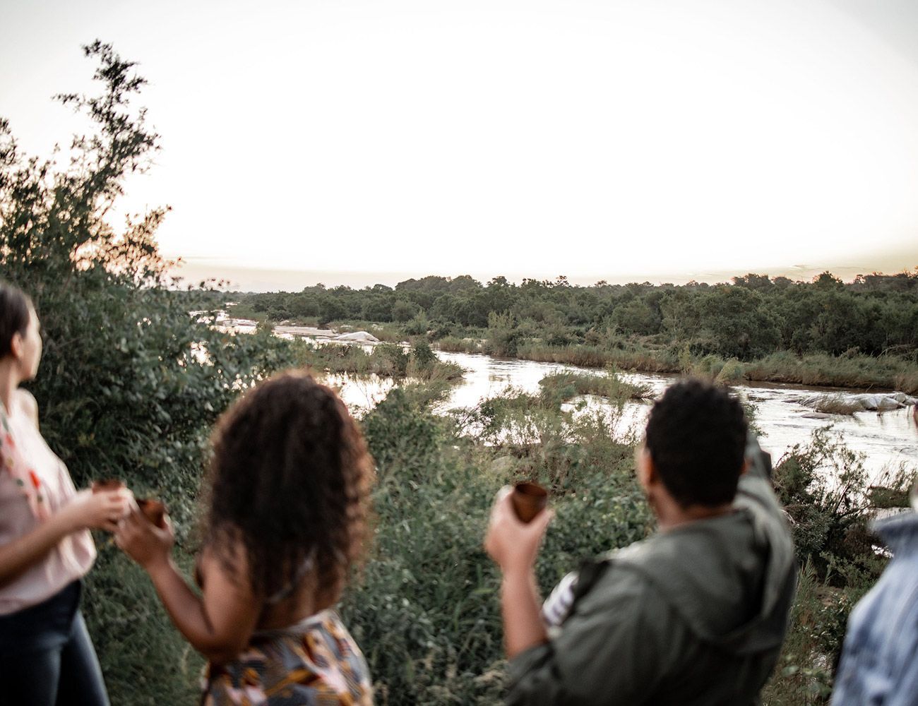 People overlooking a river at sunset, surrounded by trees and brush.