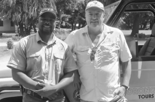 Two men standing together outdoors beside a tour vehicle, smiling at the camera.