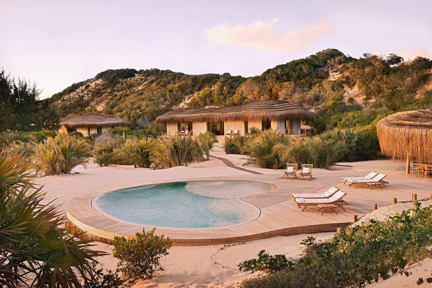 Resort pool with lounge chairs in a desert hillside setting at sunset