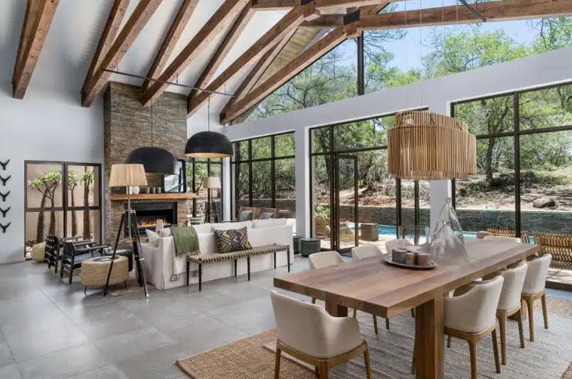 Modern open-plan living and dining room with floor-to-ceiling windows, wood beams, and mountain views
