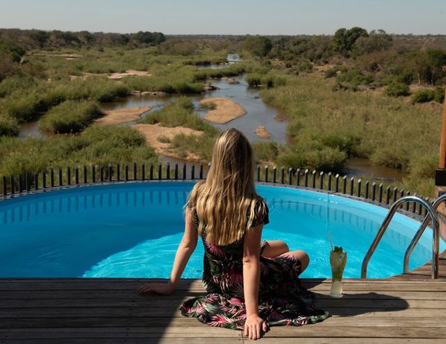 Woman sitting by a blue pool overlooking a river and green wetlands